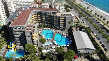 A hotel with multiple swimming pools, a beach, and a parking area.