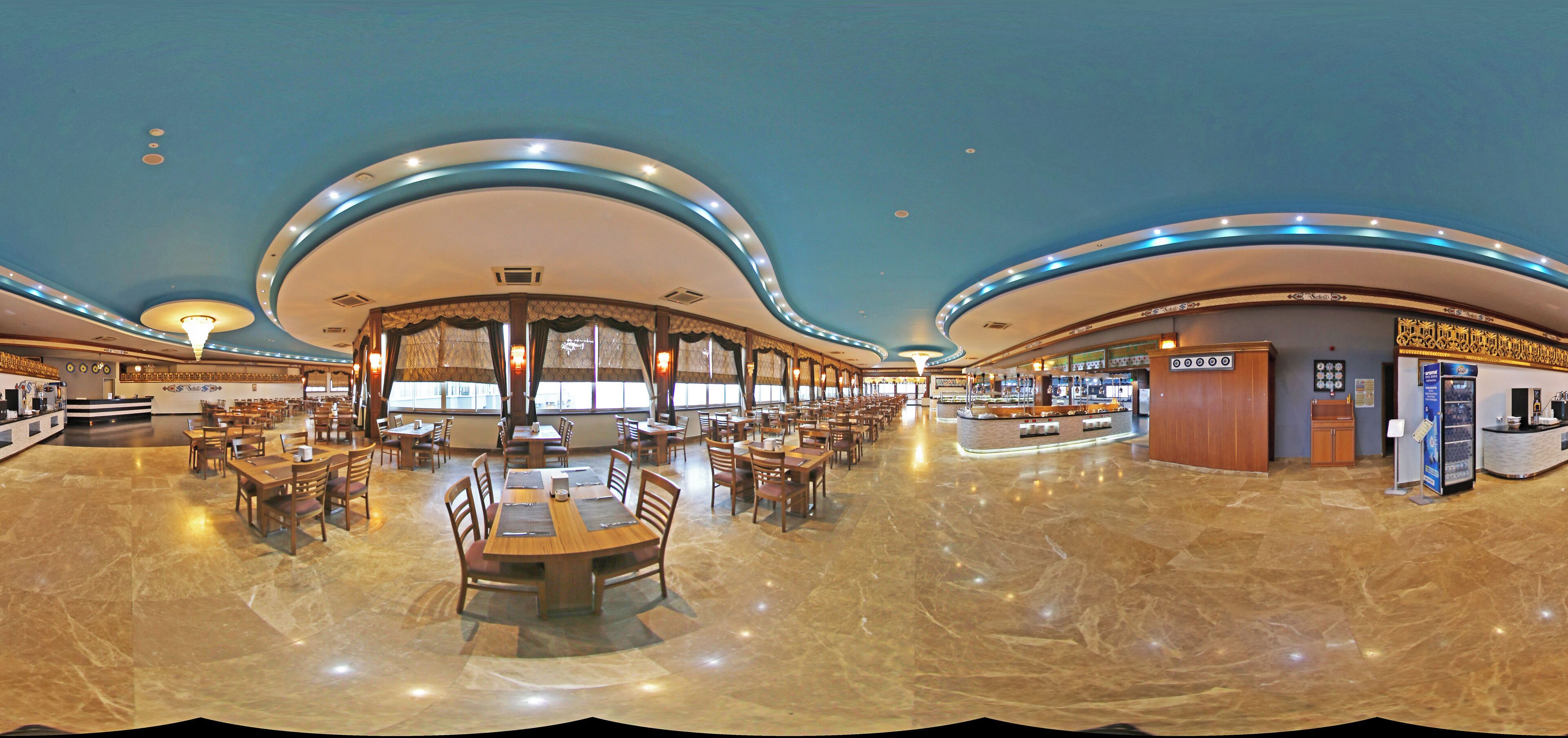 A spacious hotel lobby with a central seating area, multiple dining tables, and a reception desk.