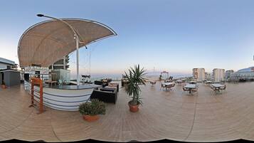 A rooftop terrace with a bar area, outdoor seating, and potted plants.