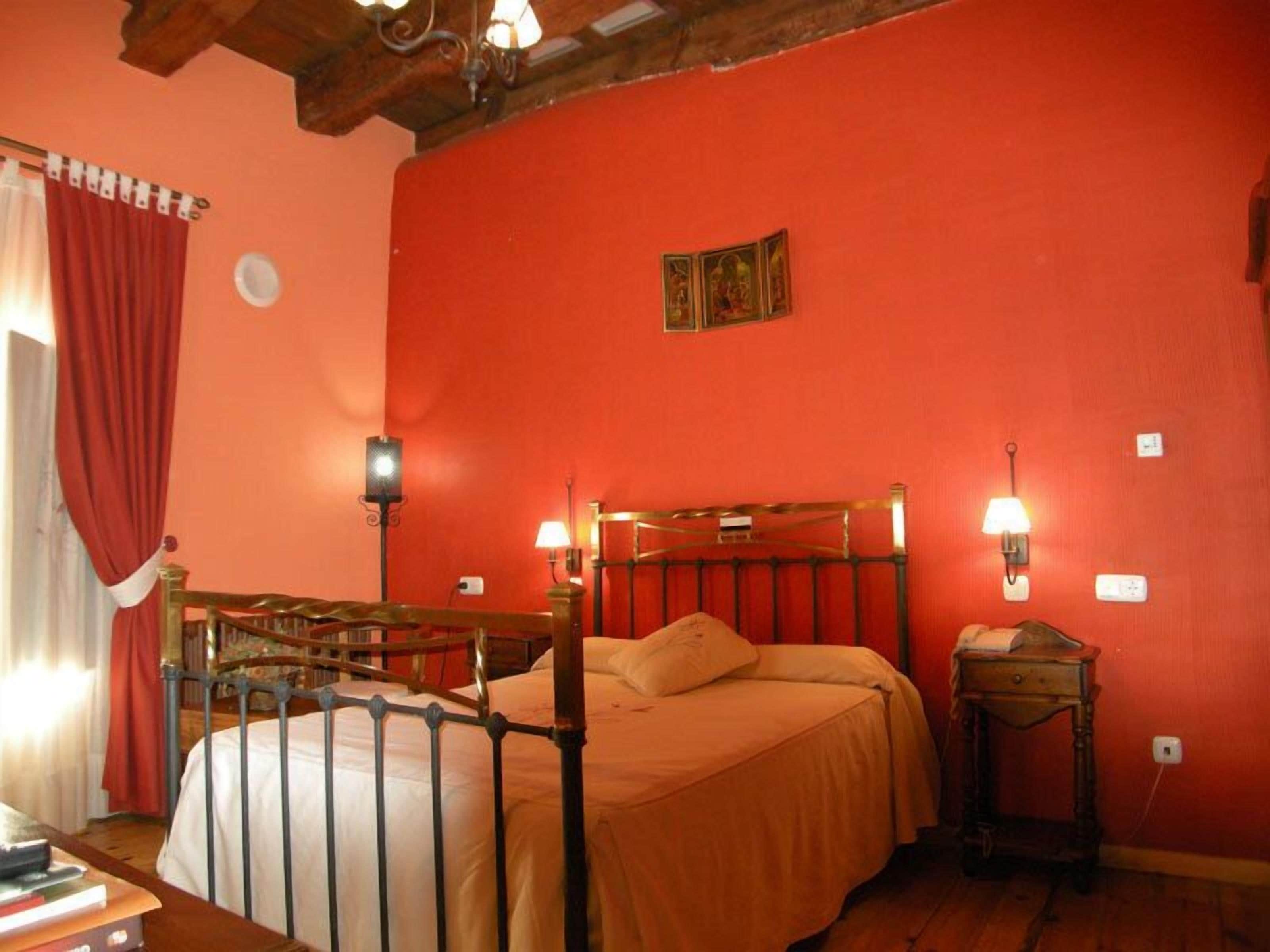 A room with a bed, two wall-mounted lamps, a small table, and a red curtain.
