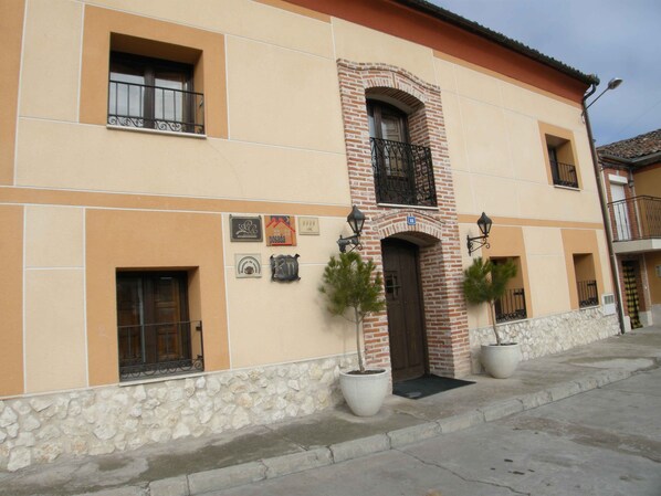 A building with a stone base, beige walls, and a brick archway. There are potted plants in front, and a door with a metal gate. - La Posada de Carmen (Chane)