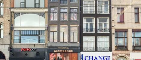 A row of multi-story buildings with storefronts, including a 'Pasta Bar' and a 'SEX Museum'.