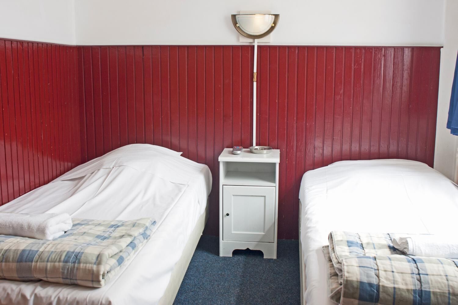 A room with two single beds, a small bedside table with a lamp, and a red wall.