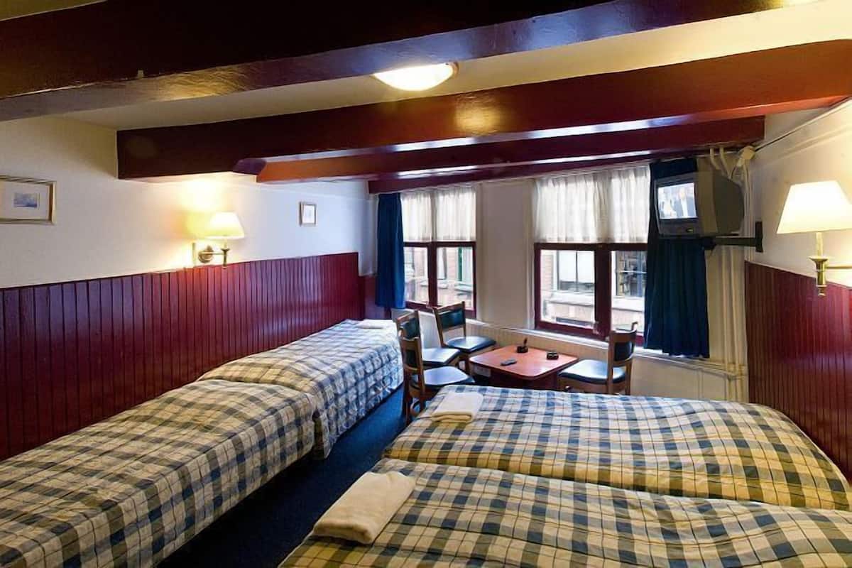 Una habitación con dos camas, una mesita, sillas y un televisor.