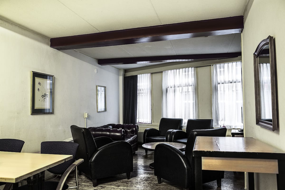 A room with a wooden ceiling, a black leather sofa, a dining table, and a window with curtains.