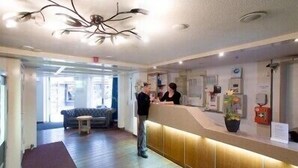 A reception area with a wooden reception desk, a sofa in the background, and a ceiling with a modern light fixture. - Hotel De Koopermoolen (Amsterdam)