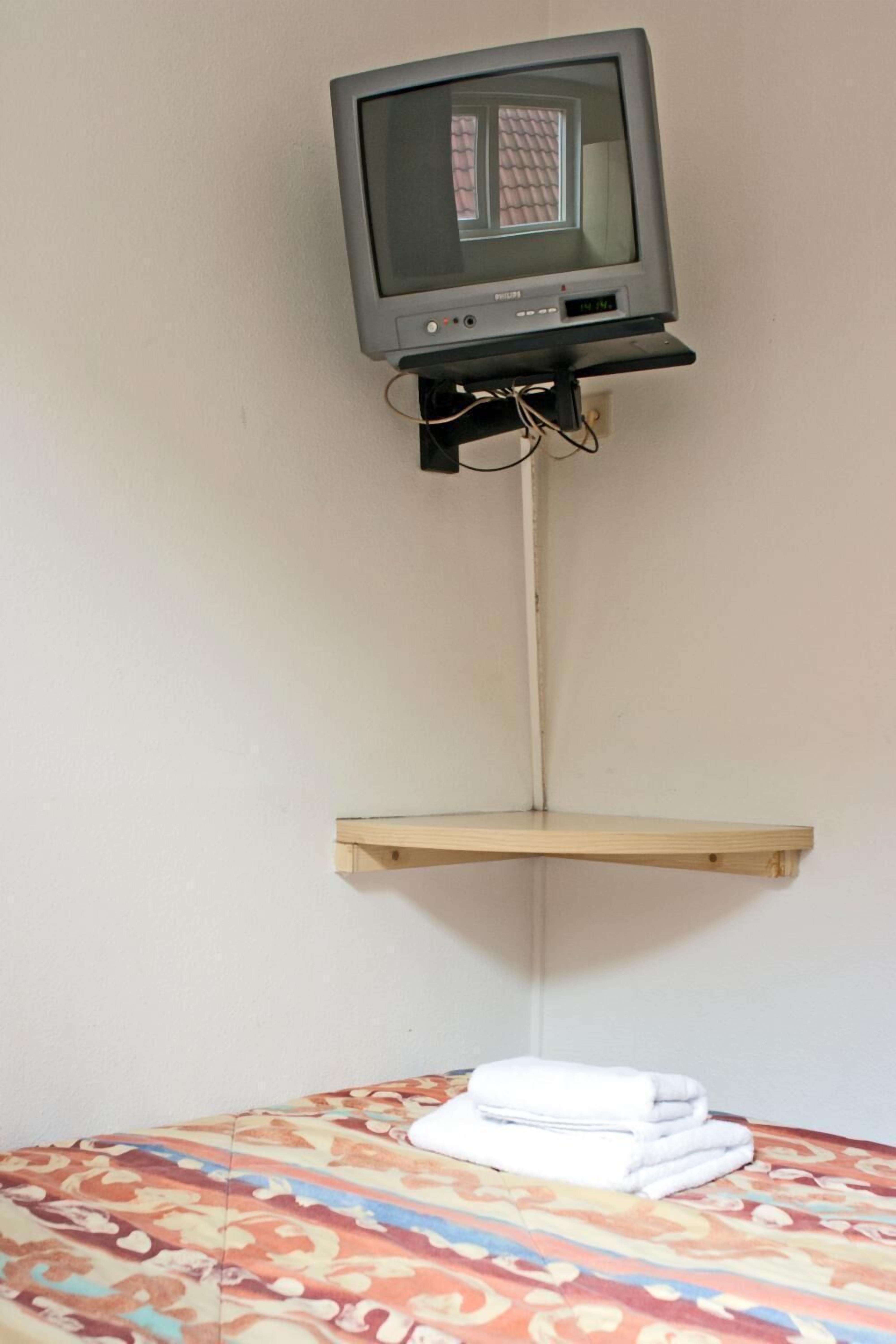 A television mounted on a wall with a wooden shelf below it.