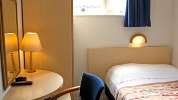 Une chambre d’hôtel avec un lit, une table ronde avec deux lampes, une chaise, une lampe de chevet et une fenêtre avec des rideaux.