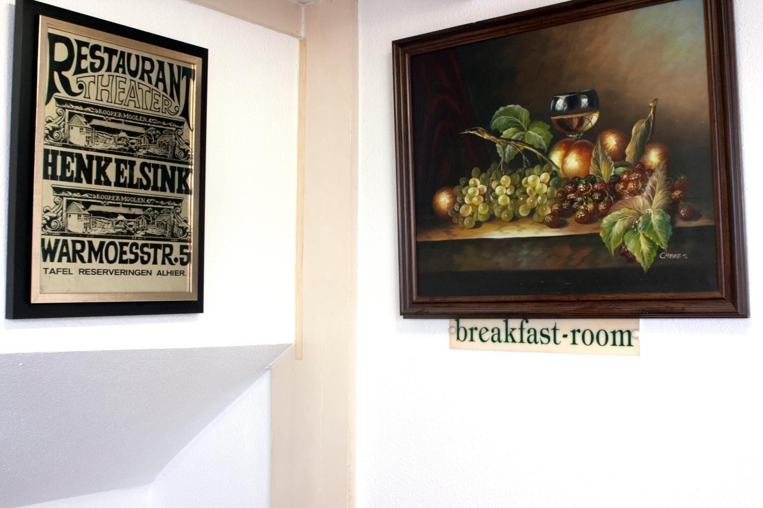 A framed vintage restaurant sign and a still life painting in a breakfast room.