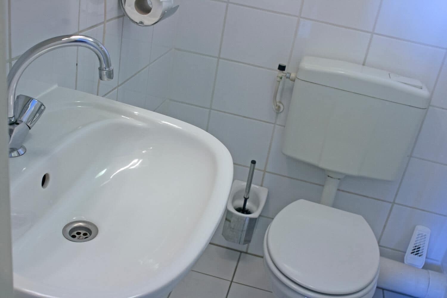 Un baño con lavamanos blanco, inodoro y soporte para papel higiénico.