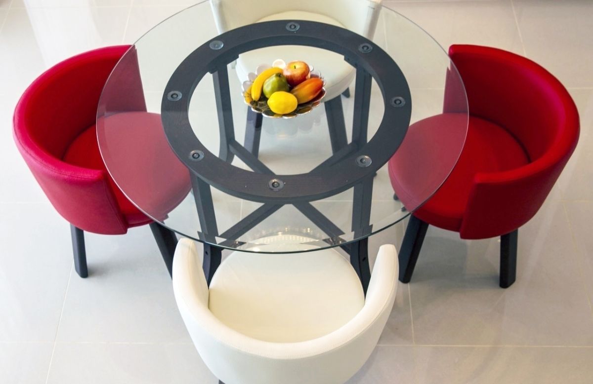 A round glass table with a central bowl of fruit, surrounded by red chairs.