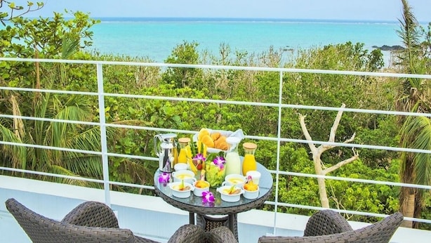 Un balcon avec des fauteuils en osier, une table avec des aliments pour le petit-déjeuner et une vue sur l’océan.