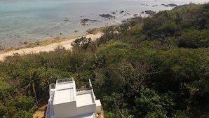 Une vue côtière avec une plage, une végétation luxuriante et un bâtiment blanc doté d’un balcon.
