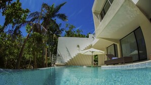 Une piscine bordée d’un bâtiment moderne, de palmiers et d’un escalier menant à un niveau supérieur.