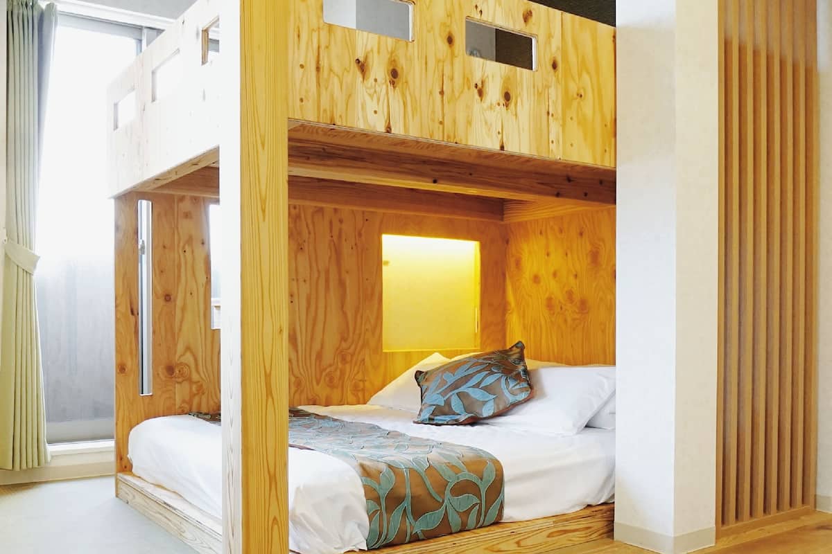 A bunk bed with a wooden headboard, a bedside table, and a window with curtains.