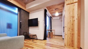 A modern living room with a grey sofa, wooden flooring, a mounted TV, and a wooden wardrobe.