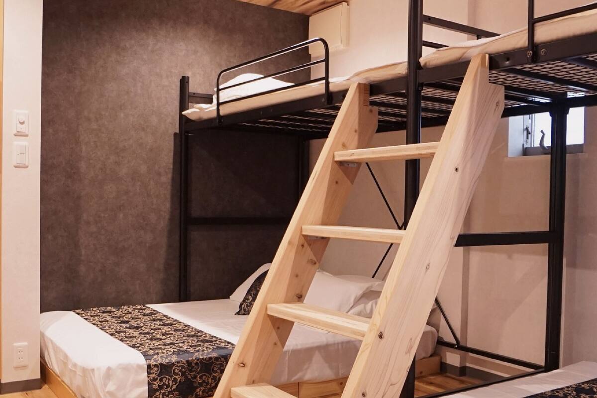A bunk bed room with a wooden ladder, two beds with patterned bedding, and a wooden floor.