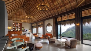 A spacious lounge area with modern furniture, a wooden ceiling, and large windows offering a view of the outdoors. - 98 Acres Resort & Spa (Ella)