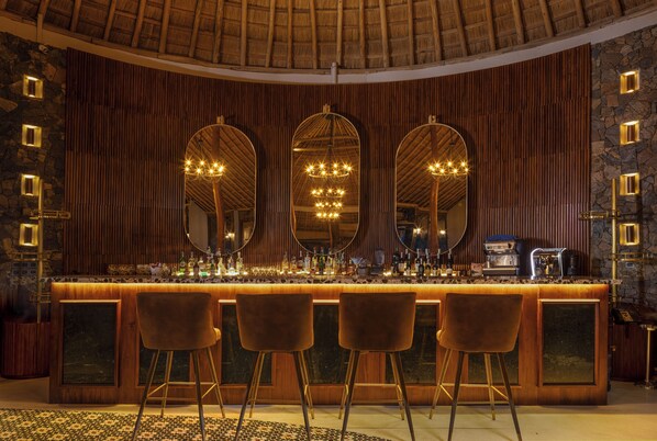 A bar area with a wooden counter, three mirrors, and a chandelier.