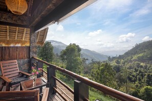 Una terraza de madera con barandilla, una silla, una mesa y un jarrón de flores.