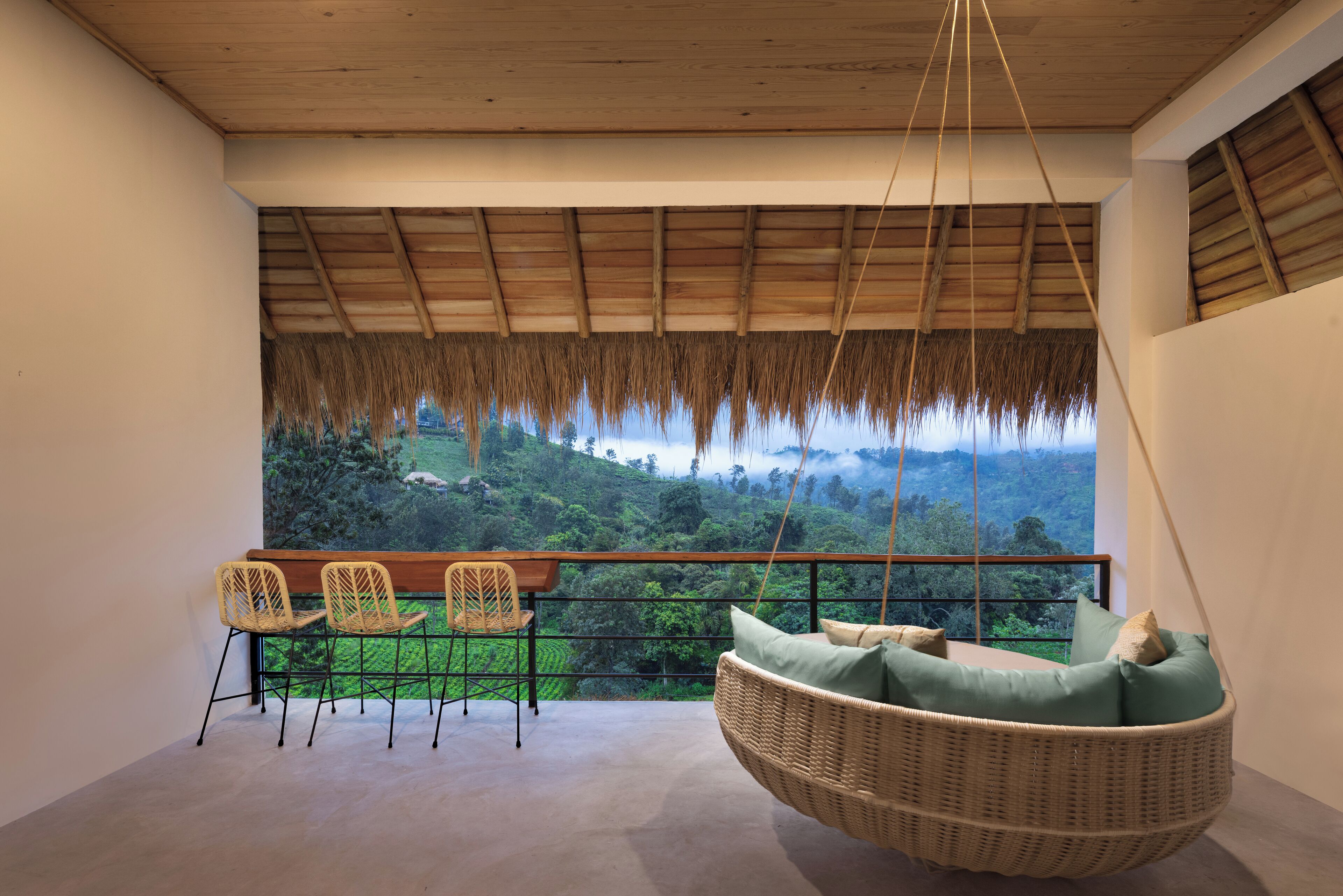 Un balcon agrémenté d’un fauteuil suspendu en osier et de deux chaises, offrant une vue sur un paysage verdoyant et luxuriant.