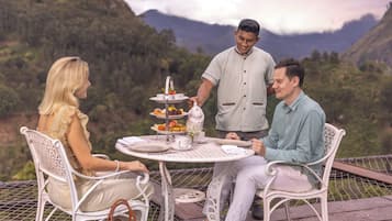 A table set outdoors with a scenic mountain backdrop, featuring a tiered dessert stand and a teapot.