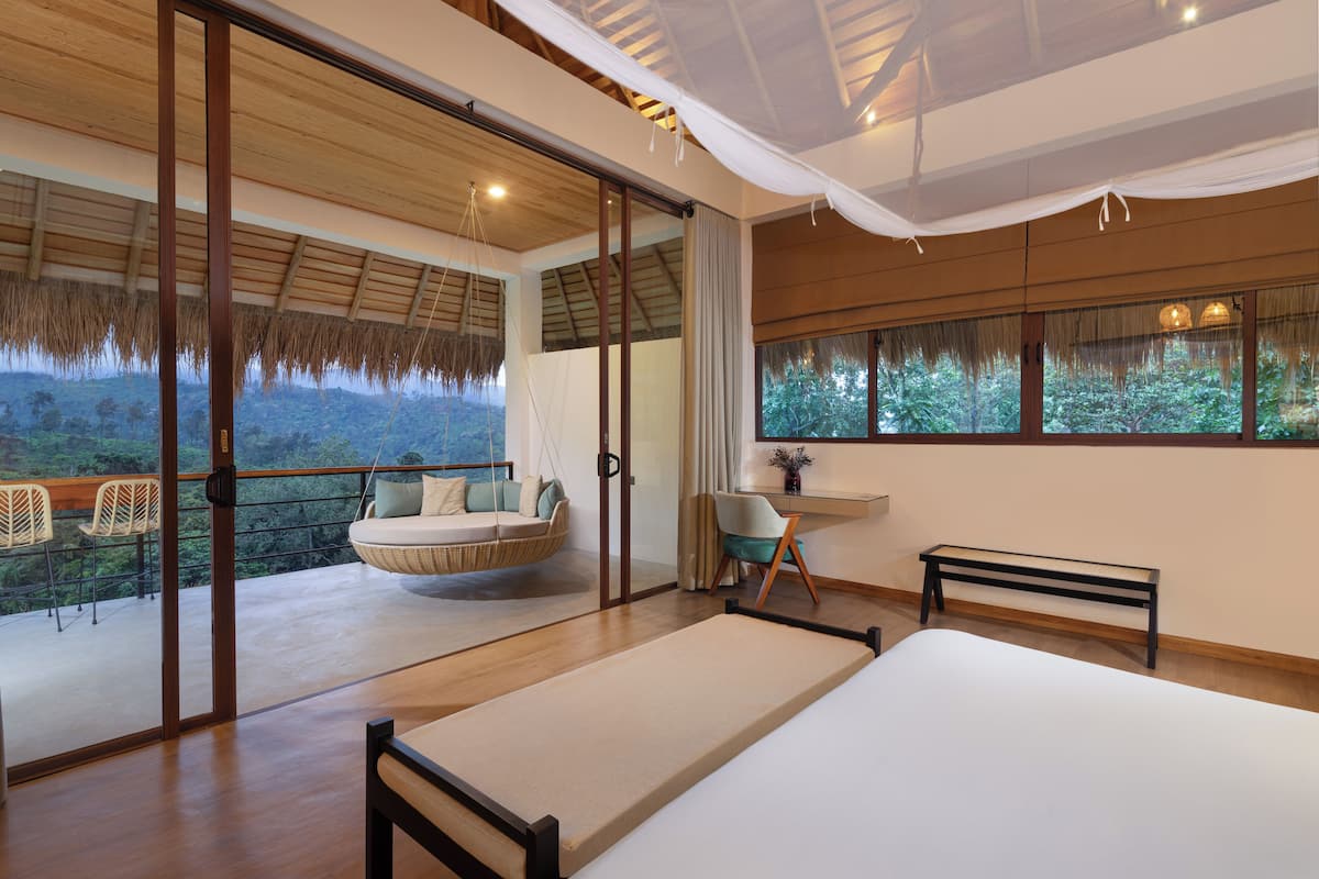 A bedroom with a bed, a hanging chair, a desk, and a view of the outdoors.