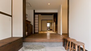 A hallway with wooden flooring, a stone accent, and three wooden stools. - Hashibaan (Kanazawa)