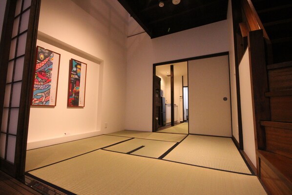 Una habitación japonesa tradicional con suelo de tatami, un celosía de papel shoji y dos cuadros en la pared.