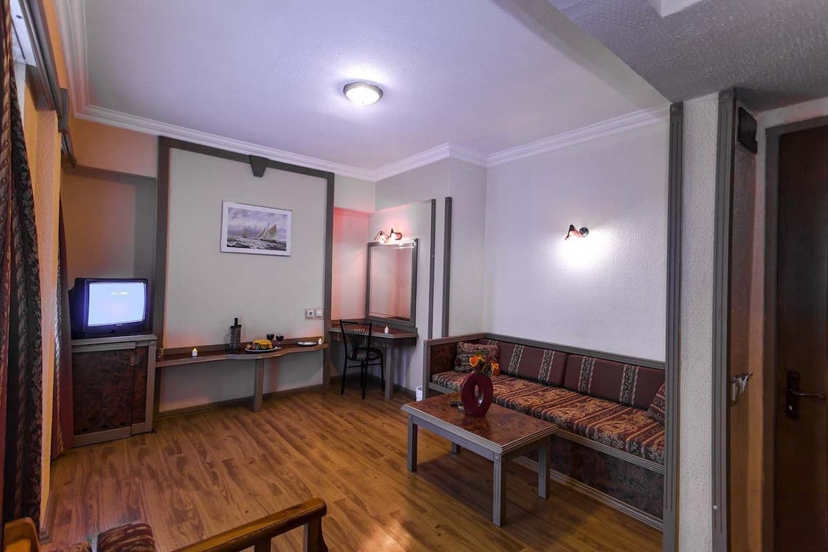 A living room with a wooden floor, a sofa, a coffee table, a TV, and a desk with a chair.