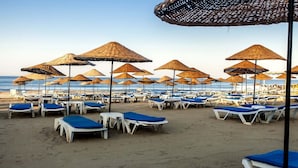 Ein Strand mit Liegestühlen und Sonnenschirmen aus Reisig.