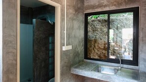 A modern bathroom with a built-in sink, a window with a view of greenery, and a wooden floor. - Aonang Lodge (Krabi)