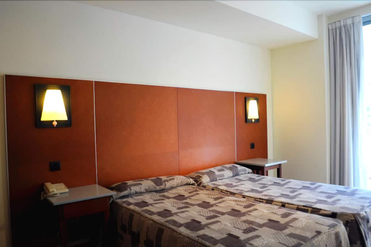 Habitación de hotel con una cama grande, dos mesitas de noche, un teléfono y dos lámparas de pared.