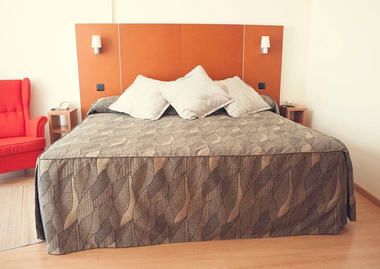 A bed with a patterned bedspread, two bedside tables with lamps, a red chair, and a wooden headboard.