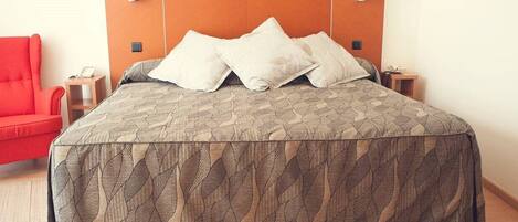 A bed with a patterned bedspread, two bedside tables with lamps, a red chair, and a wooden headboard.