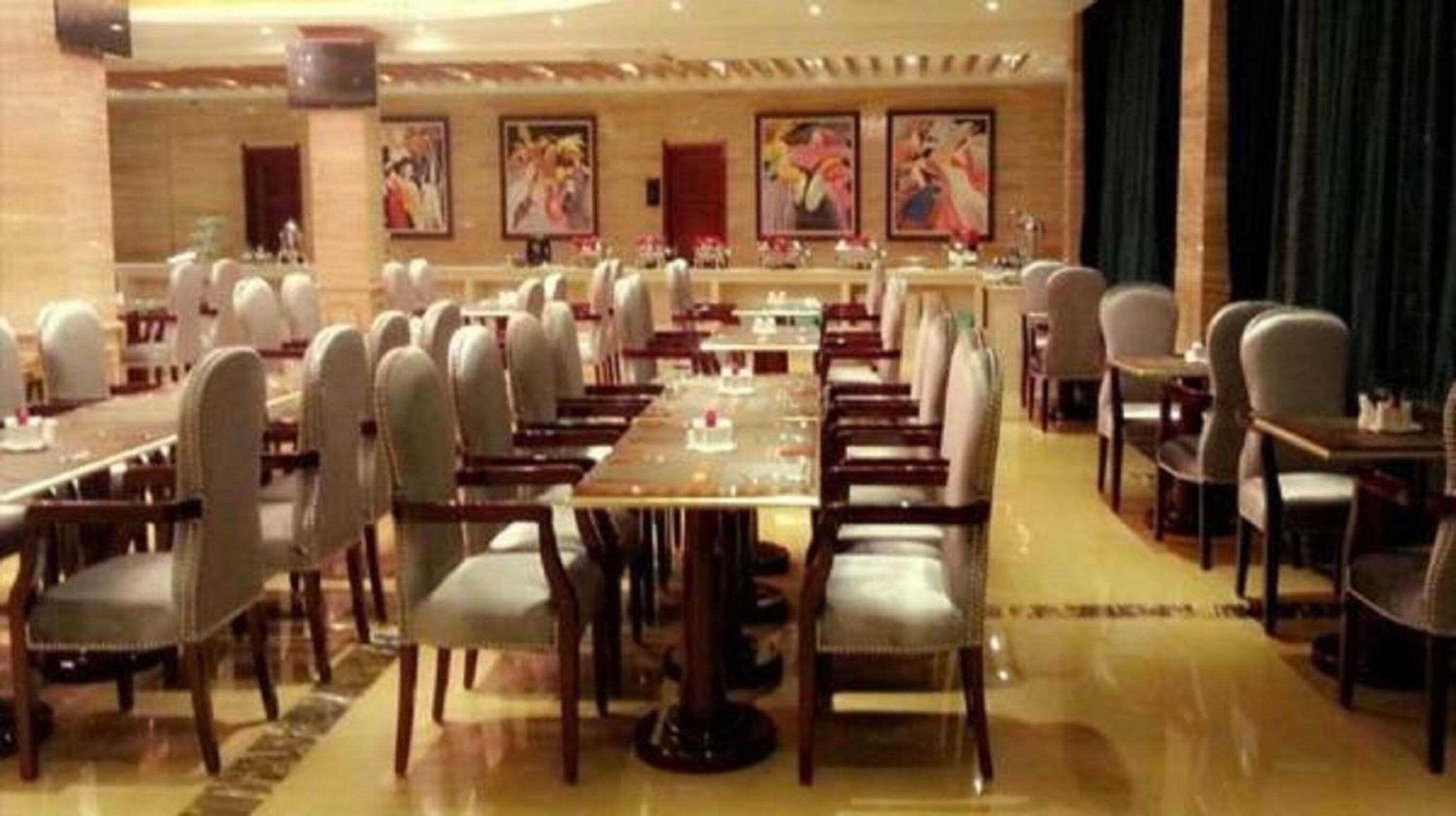 Un'ampia sala da banchetti con lunghe tavolate e sedie, opere d'arte incorniciate sulle pareti e un pavimento lucido.