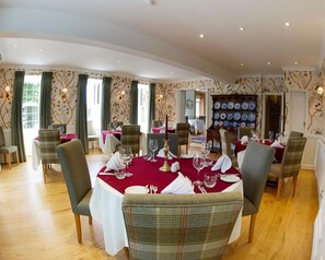 A dining area with round tables, chairs, and a wall of decorative plates. - Sherbourne House (Attleborough)