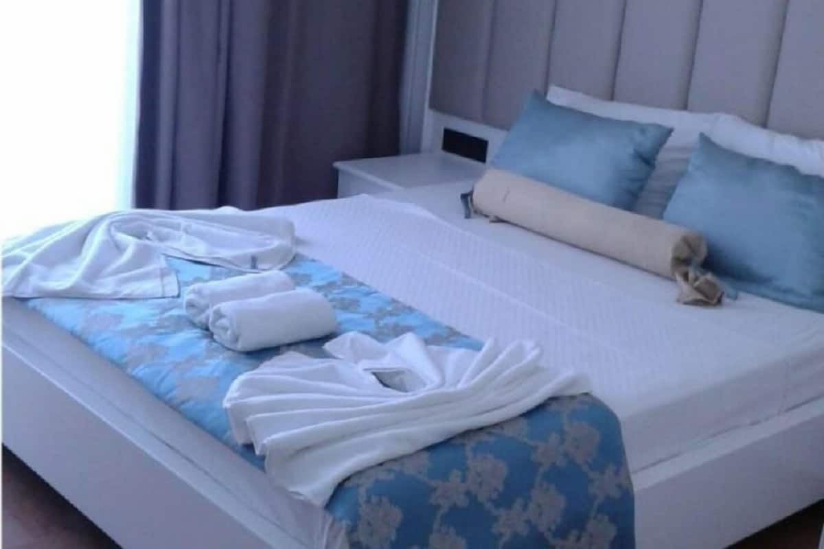 A neatly made bed with a blue and white bedspread, white pillows, and a rolled-up beige blanket.