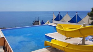 Ein Pool mit Rutsche, Meerblick und ein Gebäude mit Schild 'Barbeque'.