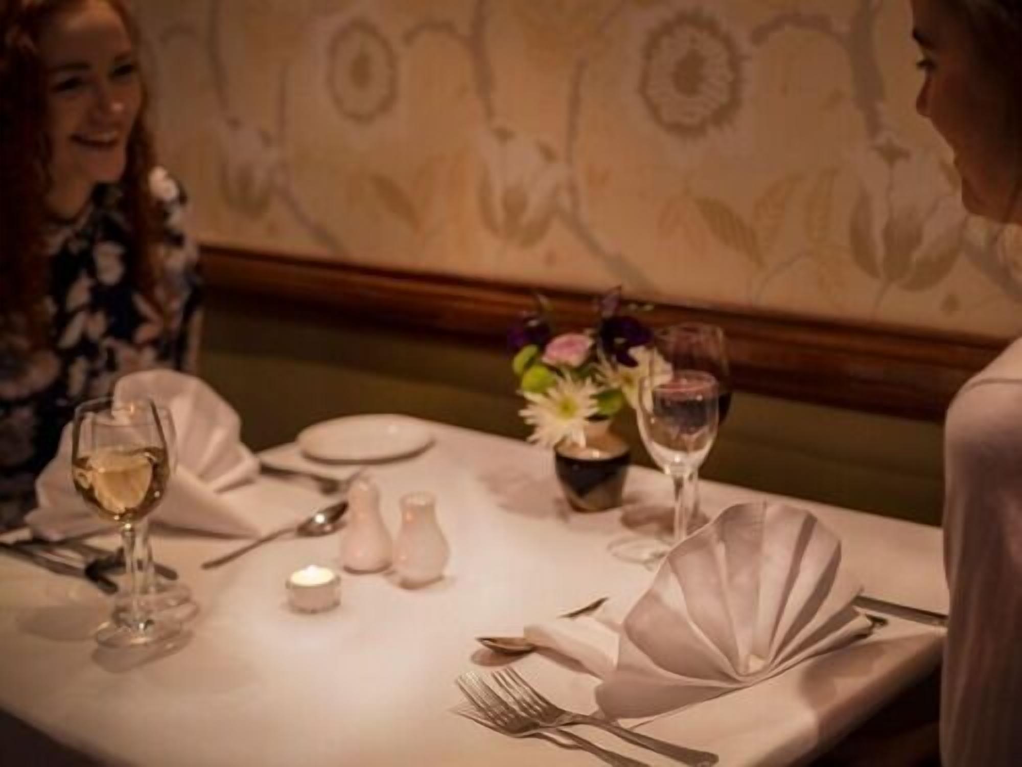 A dining table set with white tablecloth, plates, cutlery, and a vase with flowers.