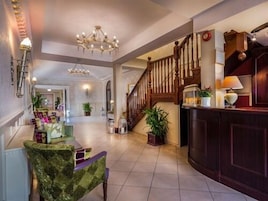 A spacious lobby with a grand staircase, a chandelier, and a reception desk.