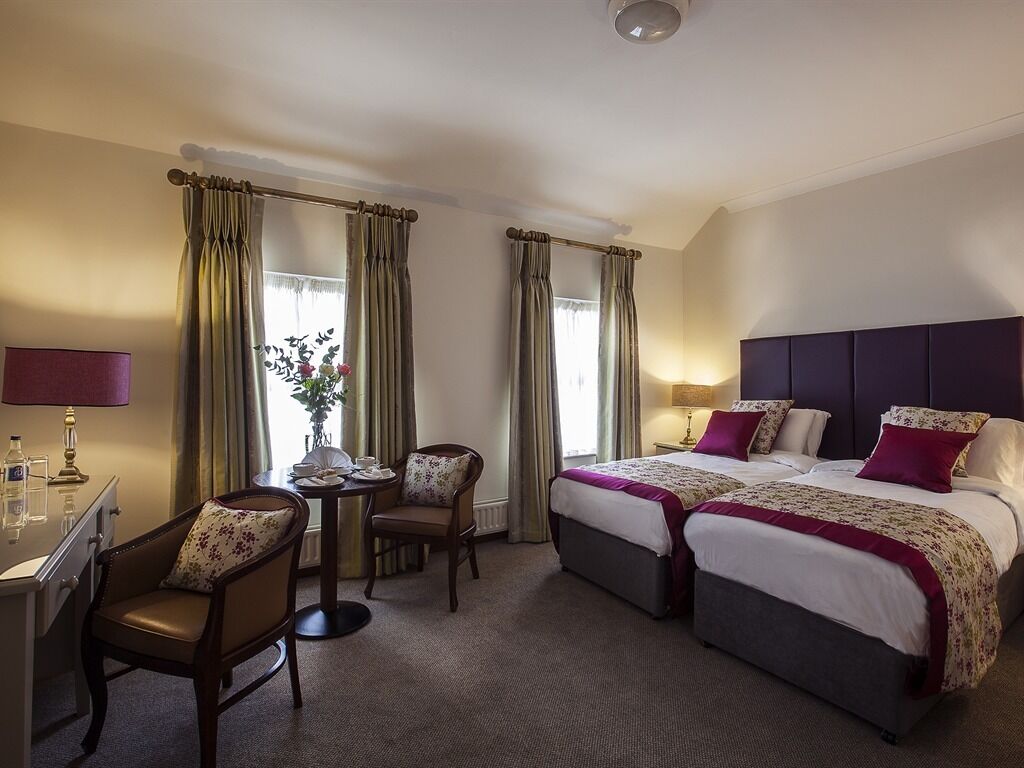 A hotel room with two beds, a desk, a chair, and a small table with a vase of flowers.