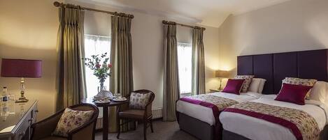 A hotel room with two beds, a desk, a chair, and a small table with a vase of flowers.