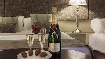 A bottle of Moët & Chandon Imperial Champagne, two glasses of champagne, and chocolate-covered strawberries on a plate, set on a table in a hotel room with patterned wallpaper and a lamp in the background.