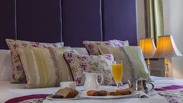Een netjes opgemaakt bed met bloemenbedrukking, een ontbijtplateau met toast, jam en sap, en een bedlampje.