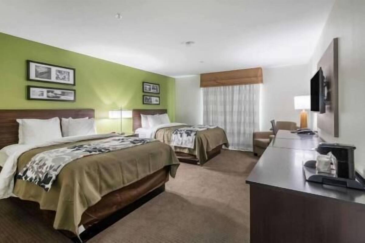 A hotel room with two beds, a desk, a chair, a TV, and framed pictures on the wall.