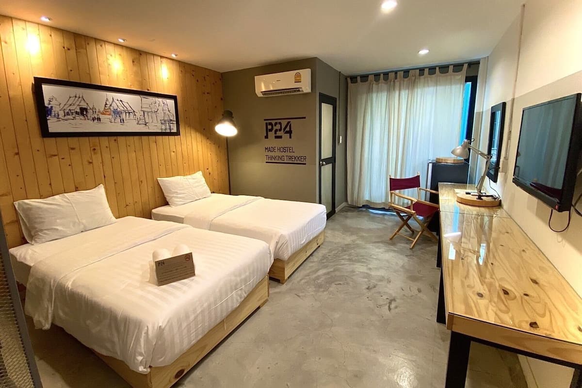 A hotel room with two beds, a desk, a chair, an air conditioner, and a framed picture on the wall.