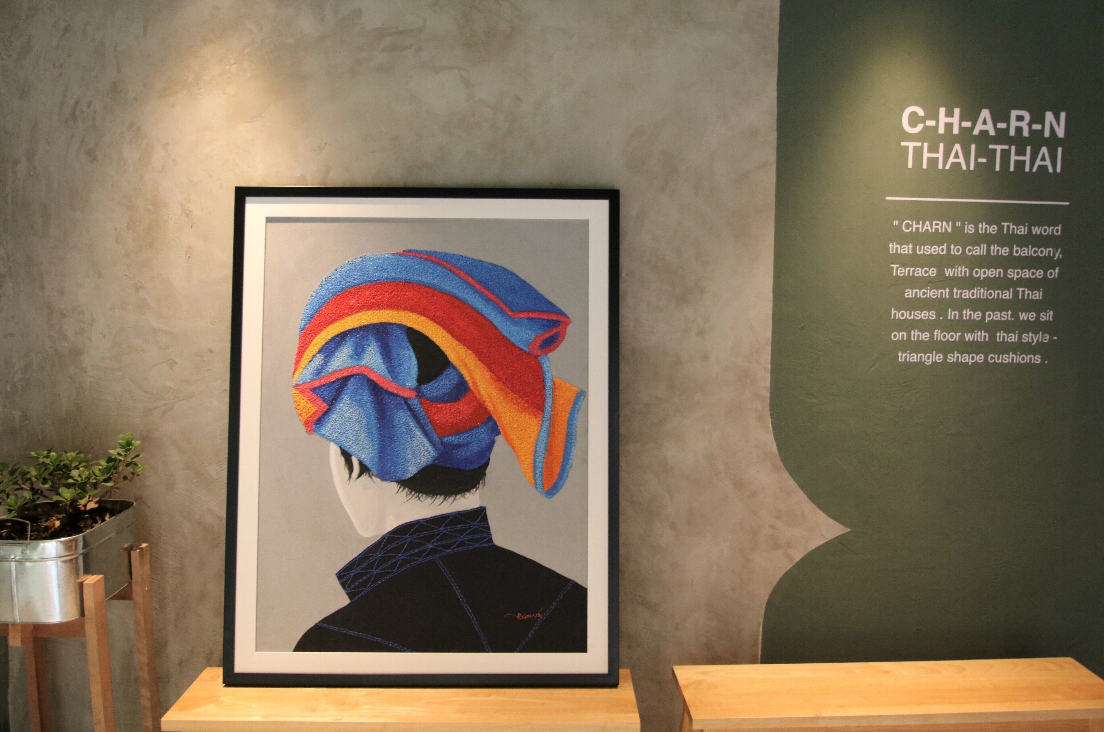 A framed artwork of a person wearing a colorful traditional Thai headdress, with a description of 'CHARN' on the wall.