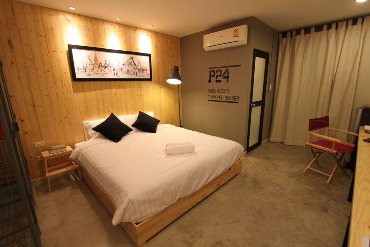 A bedroom with a wooden bed, a nightstand, a chair, and a wall-mounted air conditioner.