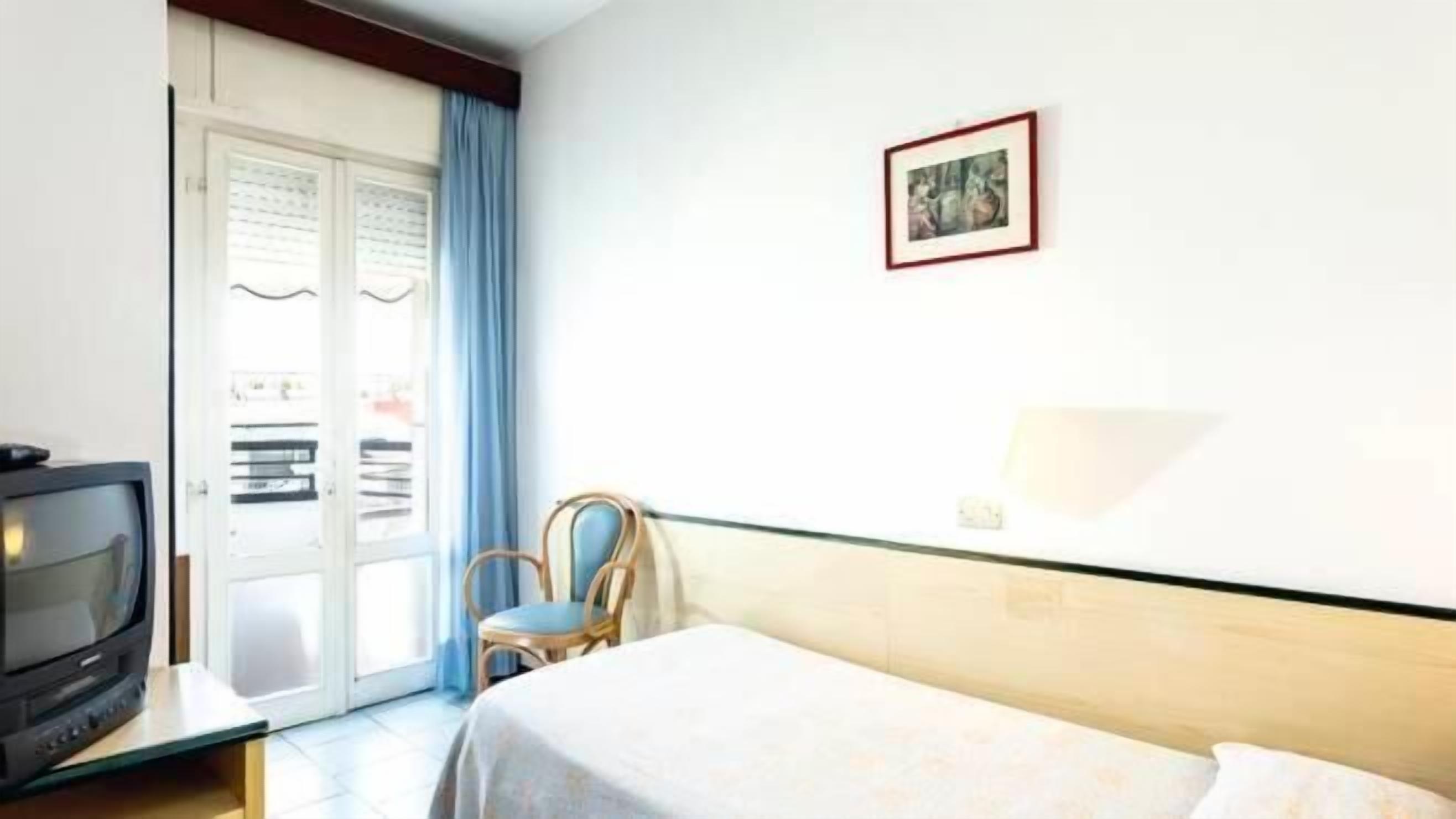 A hotel room with a bed, a television, a chair, and a door leading to a balcony.